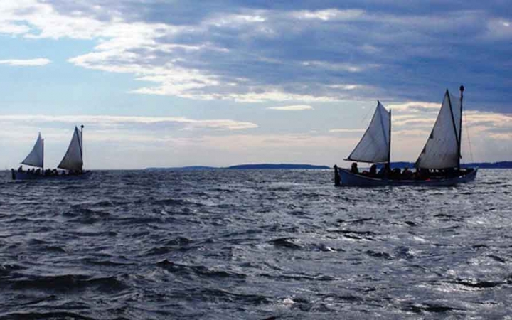 two sailboats glide in blue open water on an outward bound course in maine